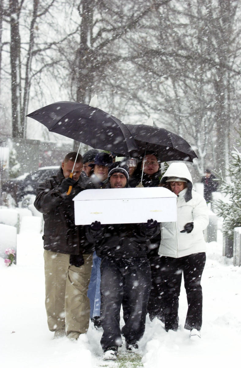 A father carries the casket of his newborn infant to a gravesite. The baby, who died shortly after birth, was born to a mother who was in prison.