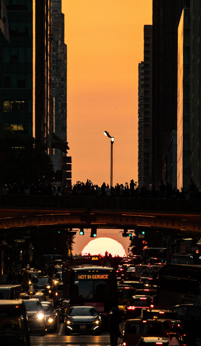 People stand on an overpass over 42nd St. in Manhattan May 30, 2023 as they watch and photograph the setting sun during the second consecutive night of Manhattanhenge. Manhattanhenge is an event during which the setting sun is aligned with the eastwest streets of the street grid of Manhattan. 